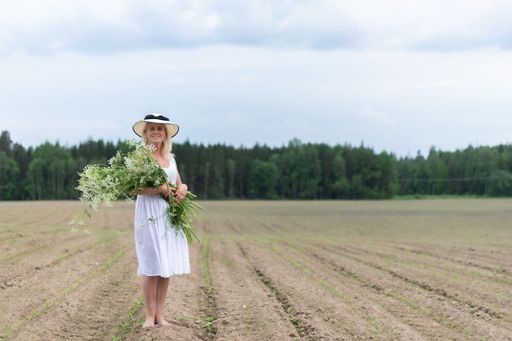 A beautiful blonde woman wearing a hat and a white dress holding flowers in a field