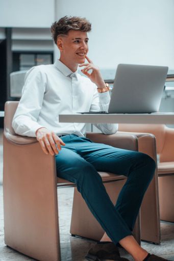 A vertical shot of a young Spanish man sitting in front of a laptop