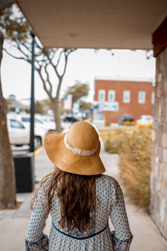 A female with a summer hat walking on the sidewalk with a blurred background shot from behind