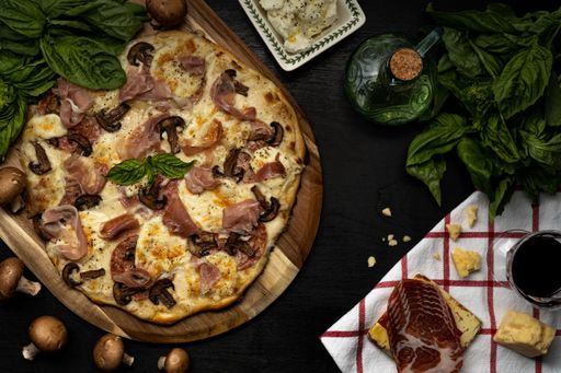 A top view of the mushroom and prosciutto pizza on a wooden board and on a table