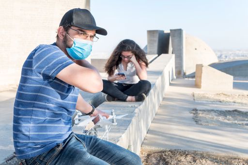 A Caucasian male wearing a medical mask sitting in a park and keeping social distance