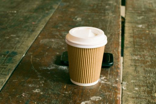 A closeup shot of a disposable cup with mobile phone a wooden table