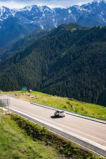 A vertical shot of a car driving on road surrounded by mountains