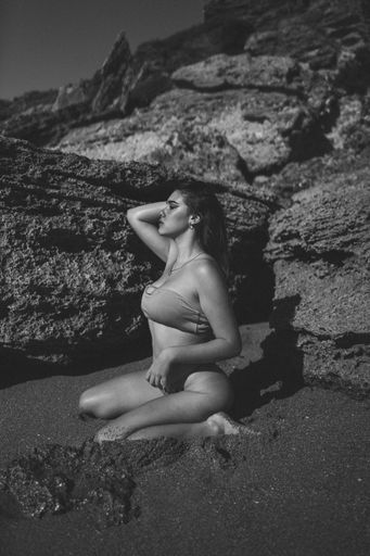 A Caucasian female brunette in bikini sitting in sexy pose on sandy beach in Cadiz, Spain, grayscale