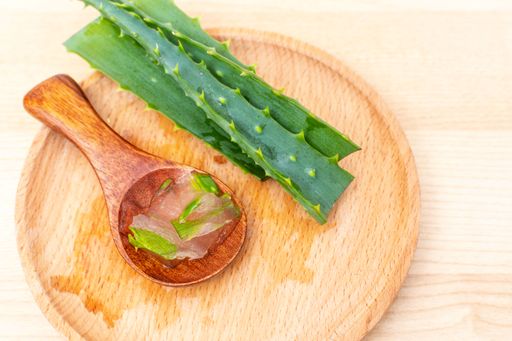 A close-up shot of aloe leaves and gel in a wooden spoon on a wooden tray