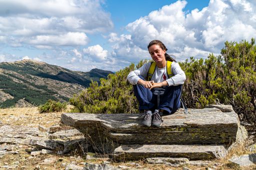 A blonde Hispanic female with wavy hair, sitting on a rock and resting on a mountain hiking trail