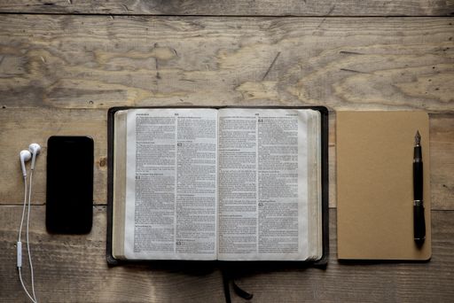 An overhead shot of opened bible in the middle of a notebook and a smartphone on a wooden surface