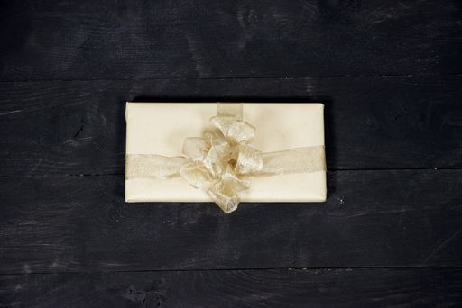 An aerial shot of a present with a golden ribbon and a bow on a wooden surface