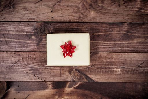 An overhead shot of a present with a red bow on a wooden surface
