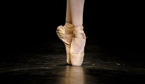The feet of a Ballerina dancing on a black dance floor in closeup
