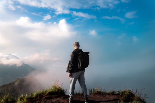 A scenic view of a male person standing on top of a volcanic mountain with clouds in front of him