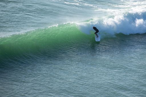 View of bearded surfer riding perfect long wave at Piha beach, Auckland, New Zealand. Auckland, New Zealand - February 21, 2021