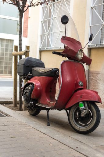 A vertical shot of red Italian Vespa scooter parked on street