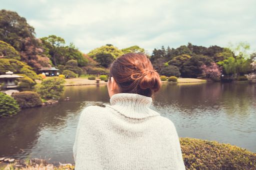 A female enjoying the view of a pond and trees with a cloudy sky in the background shot from behind