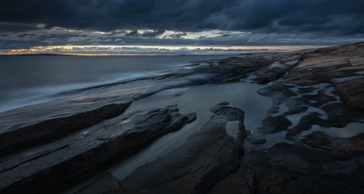 A wide shot of rocks on the shore near the sea under a cloudy sky