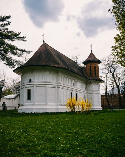The vertical view of St. George's church in the grass field under the cloudy sky in Mogosoaia