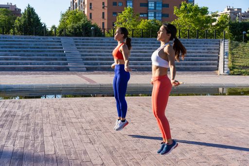 Two young Caucasian athletic female friends doing exercises and jumping outside - healthy lifestyle concept