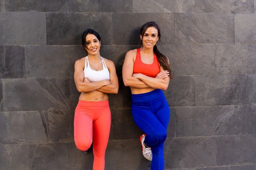 Two young Caucasian athletic female friends doing exercises and stretching outside - healthy lifestyle concept