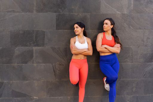 Two young Caucasian athletic female friends doing exercises and stretching outside - healthy lifestyle concept