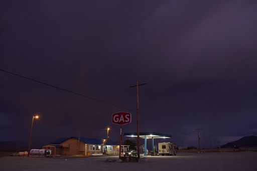 A gas station near wire poles under a cloudy sky at night time