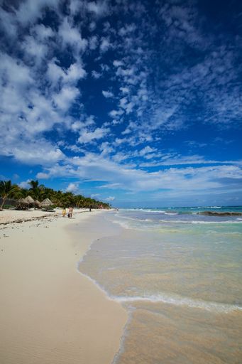 A vertical shot of low sea tides washing up ashore at Tulum, Mexico under a bright cloudy sky