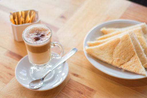 A high angle shot of a cup of Caffe macchiato next to pastries and sugar packets on a wooden surface