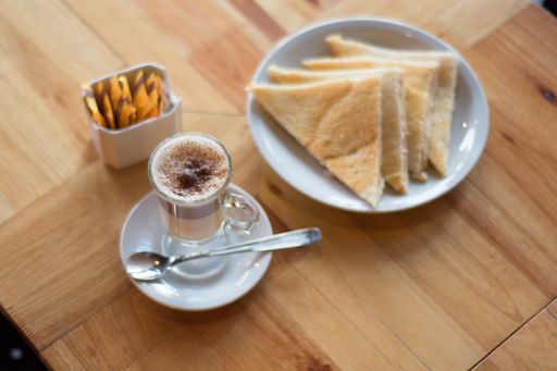 A high angle shot of a cup of Caffe macchiato next to pastries and sugar packets on a wooden surface