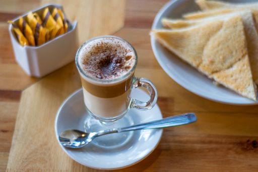 A high angle shot of a cup of Caffe macchiato next to pastries and sugar packets on a wooden surface