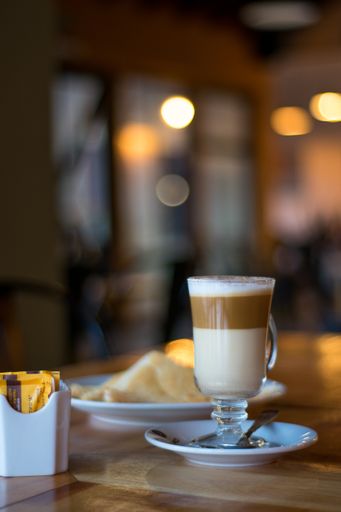 A vertical shot of a cup of Caffe macchiato next to pastries and sugar packets on a wooden surface