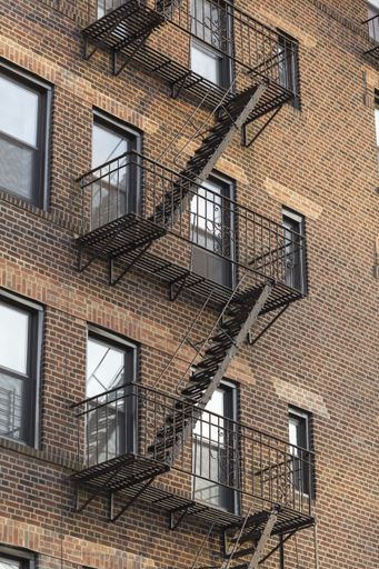 A vertical shot of a brown apartment building with metal staircases during daytime
