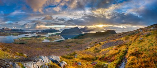 A panoramic shot of grassy hills and mountains near water under a blue cloudy sky in Norway