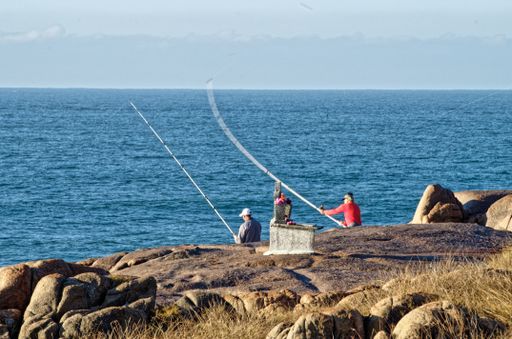 A beautiful shot of two fishermen sitting at the seashore  and holding fishing rods
