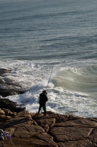 A vertical shot of a fisherman holding a fishing rod and trying to catch fish in strong waves