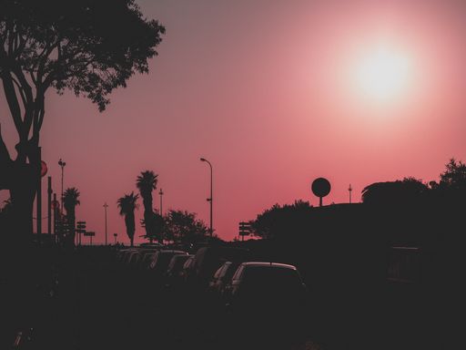 A silhouette of trees and cars with light pink and a purple sky in the background