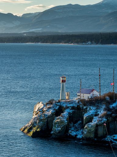 A vertical shot of a lighthouse on the rocky Vancouver Island in Canada during sunset