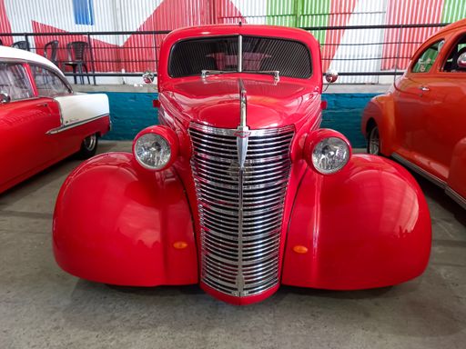 Old red Chevrolet Chevy Master coupe 1938 by GM in a warehouse yard. Street hot rod. Front view. Grill. Chromes. Expo Fierro 2022 classic car show