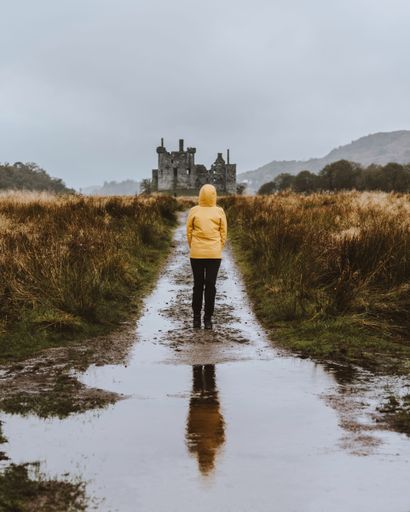 A vertical shot of the woman in a yellow jacket looking at Kilchurn Castle. Dalmally, UK.