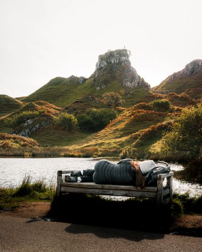A woman laying on a bench with a view of the sea and highlands in Skye island, Scotland.