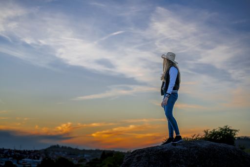 A European female with cowboy hat standing on a rock and watching the sunset