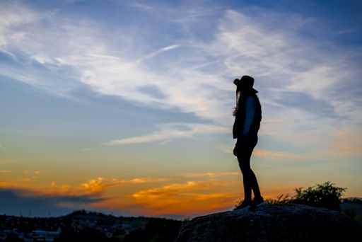 A European female with cowboy hat standing on a rock and watching the sunset