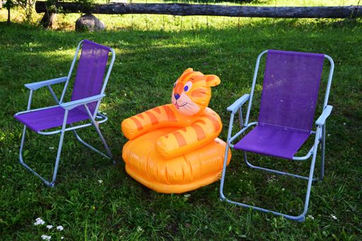 An inflatable tiger chair between two blue camping folding chairs in lush garden