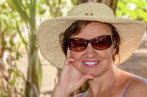 Beautiful Brazilian woman, in her 60s. Wearing glasses and hat.