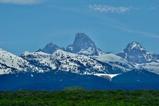 A scenic view of mountain range covered with trees and snow under a bright cloudy sky
