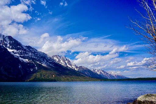 A breathtaking voew of a clean mountain lake surrounded by peaks covered with snow under a bright cloudy sky