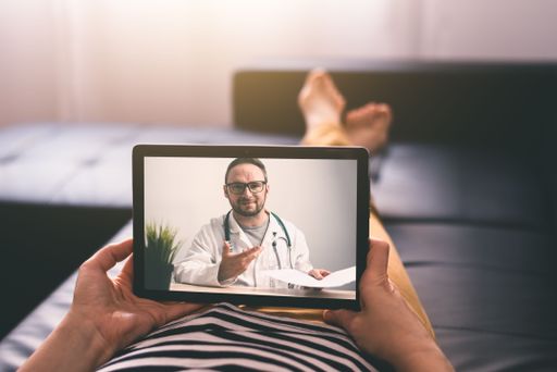 Woman lying on a sofa at home and talking with a doctor online using digital tablet. Telemedicine concept.