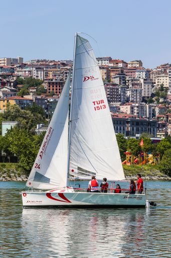 A vertical shot of people on a sailing boat and buildings in the background