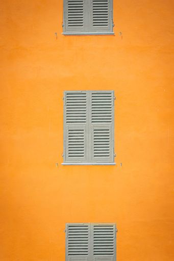 A minimalist and symmetrical photo of old, vintage looking windows on a yellowwall