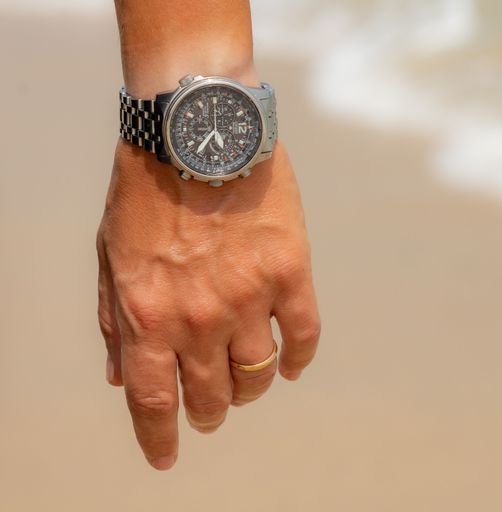 A closeup of man's hand with an engagement ring and watch on beige background