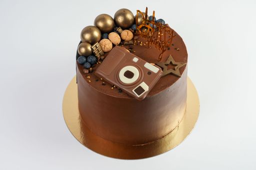 The birthday chocolate cake with golden balls  and  camera shape candy decoration isolated on white background, studio shot