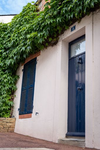 The Front of an old house covered partially with ferns, between the up and downtown of Pornic
